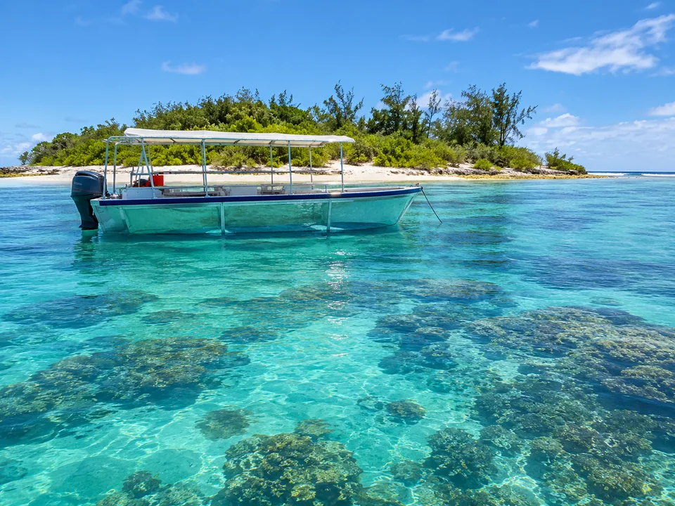 Ein kleines Glasbodenboot auf einer türkisfarbenen Lagune neben einer flachen grünen Koralleninsel